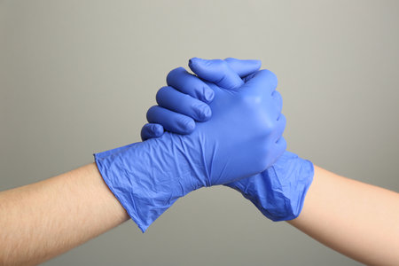 People in medical gloves shaking hands on gray background, closeup