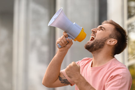 Emotional young man with megaphone outdoors. protest leaderの写真素材