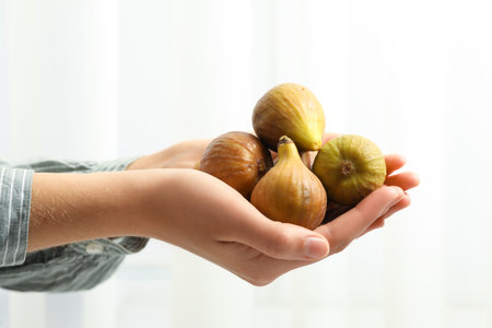 Woman holding tasty raw figs on light background, closeupの写真素材