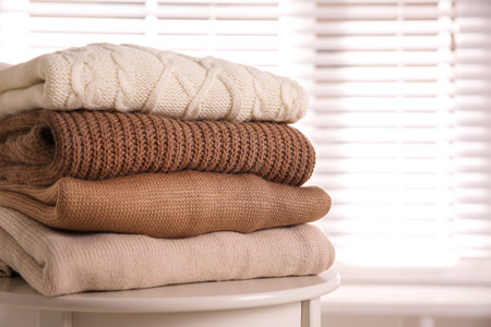 Stack of folded warm sweaters on white table indoors, closeupの写真素材