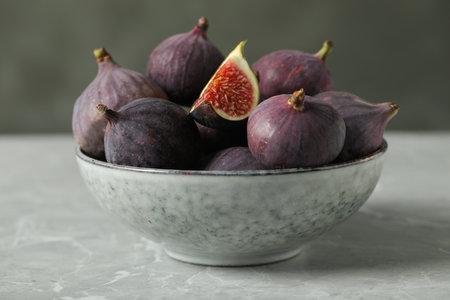 Tasty raw figs in bowl on light gray marble table, closeup