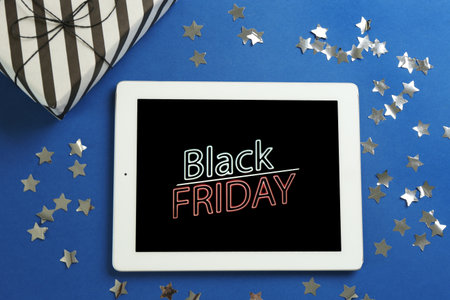 Tablet with Black Friday announcement, confetti and gift on blue background, flat layの写真素材