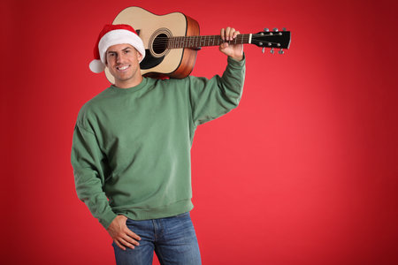 Man in Santa hat with acoustic guitar on red background, space for text. christmas musicの写真素材
