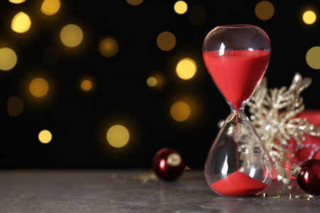 Hourglass with flowing sand and decor on gray table against blurred lights, space for text....