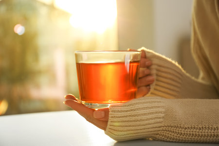 Woman holding glass cup of tea at table at home, closeupの写真素材