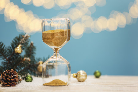 Hourglass, fir tree twigs and decor on white table against blurred lights, space for text. christmas...