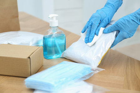 Woman cleaning parcel with wet wipe on wooden table, closeup.の写真素材
