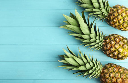Fresh ripe juicy pineapples on light blue wooden table, flat lay. Space for text