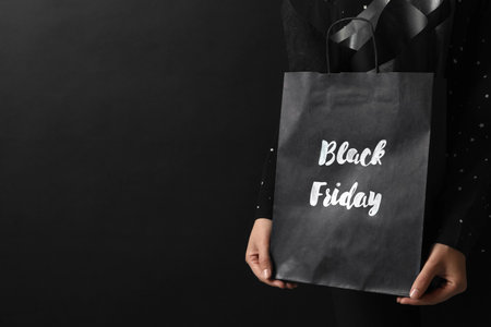 Woman holding shopping bag with words Black Friday on dark background, closeup. Space for textの写真素材