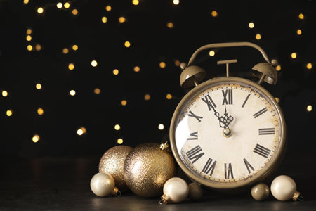 Vintage alarm clock with decor on black table against blurred Christmas lights, closeup. New Year...