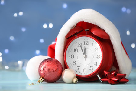 Alarm clock with decor on light blue wooden table against blurred Christmas lights, closeup. New...