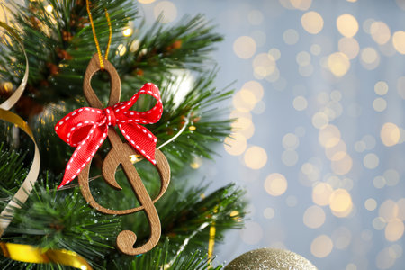 Wooden music note with red bow hanging on Christmas tree against blurred lights. Space for textの写真素材