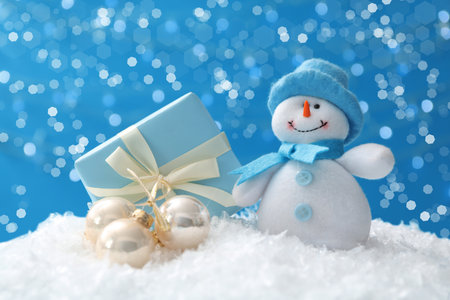 Cute snowman, Christmas balls and gift on snow against blue background, bokeh effectの写真素材