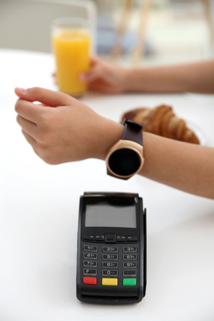 Woman using smart watch for contactless payment via terminal in cafe, closeupの写真素材