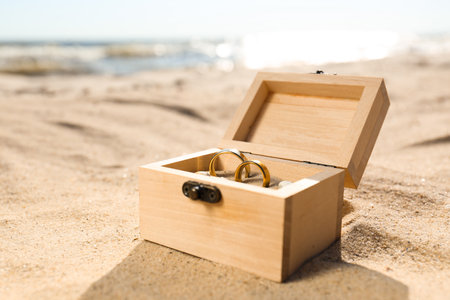 Beautiful wooden box with gold wedding rings on sandy beach