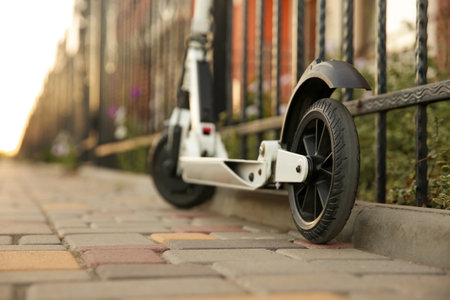 Modern electric kick scooter near metal fence outdoors, closeup