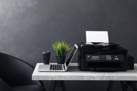 New modern printer, laptop and cup of drink on grey table indoors