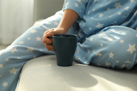 Woman in pajamas with cup sitting on sofa at home, closeupの写真素材