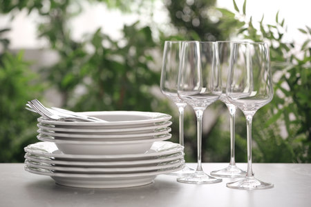 Set of clean dishware, cutlery and wineglasses on grey table against blurred backgroundの写真素材