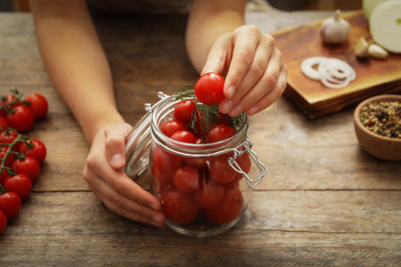 Woman putting tomatoes into glass jar at wooden kitchen table, closeup. Pickling vegetablesの写真素材