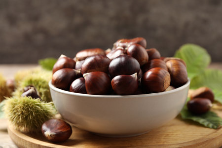 Fresh sweet edible chestnuts in bowl on wooden boardの写真素材