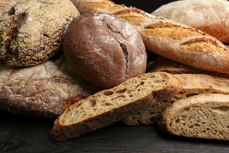 Different kinds of fresh bread on black wooden table, closeupの写真素材