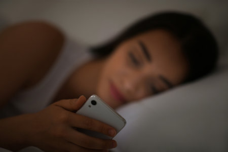 Young woman with nomophobia using smartphone in bed at night, focus on hand. Insomnia conceptの写真素材