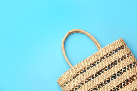 Elegant woman's straw bag on light blue background, top view. Space for text