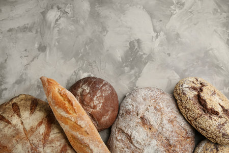 Different kinds of fresh bread on gray table, flat lay. Space for text