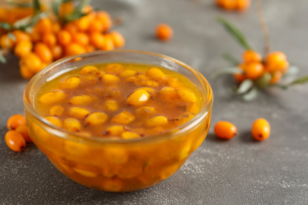 Delicious sea buckthorn jam and fresh berries on gray table, closeup