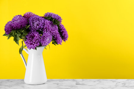 Beautiful asters in jug on table against yellow background, space for text. autumn flowersの写真素材