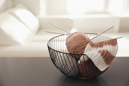 Yarn balls and knitting needles in metal basket on gray table indoors, space for text. creative...