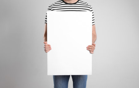 Man holding blank poster on light gray background, closeupの写真素材