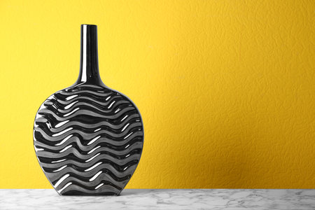 Stylish black ceramic vase on white marble table against yellow background. Space for textの写真素材