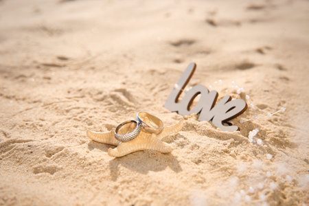 Starfish with gold wedding rings and word Love on sandy beachの写真素材