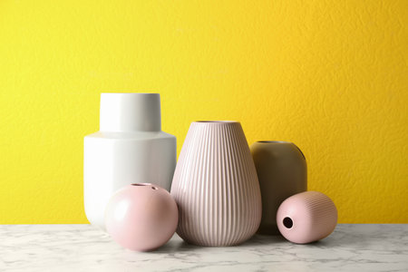 Stylish ceramic vases on white marble table against yellow backgroundの写真素材