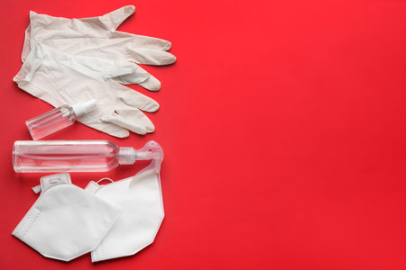 Flat lay composition with medical gloves, masks and hand sanitizers on red background. Space for textの写真素材