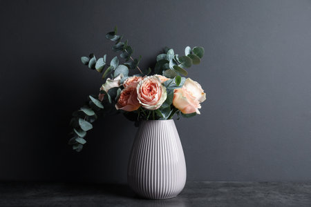 Bouquet of beautiful flowers and eucalyptus branches in vase on table against black backgroundの写真素材