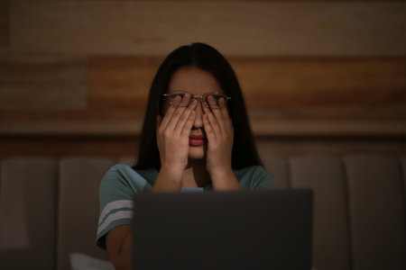 Young woman with nomophobia rubbing her eyes while using laptop at home late in the evening. Insomnia conceptの写真素材