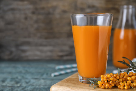 Delicious sea buckthorn juice and fresh berries on light blue table, closeup. Space for textの写真素材