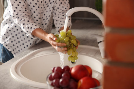 Woman washing fresh grapes in kitchen sink, closeupの写真素材