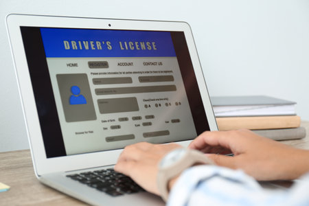 Woman using laptop to fill driver's license application form at table in office, closeupの写真素材