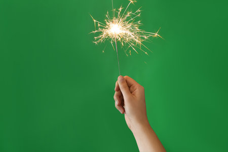 Woman holding bright burning sparkler on green background, closeupの写真素材
