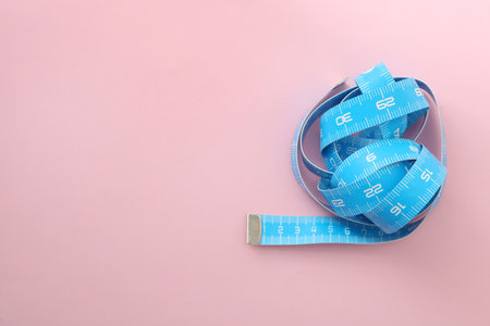 Light blue measuring tape on pink background, top view. Space for text