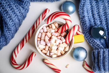 Cup of tasty cocoa with marshmallows, candy canes and Christmas balls on white table, flat layの写真素材