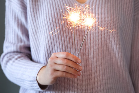 Woman in purple sweater holding burning sparklers, closeup