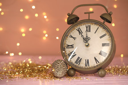 Vintage clock with decor on pink table against blurred Christmas lights, closeup. New Year count...