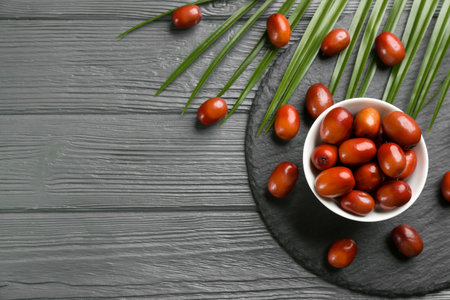 Palm oil fruits in bowl on gray wooden table, flat lay. Space for text