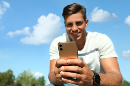 Handsome man using modern mobile phone outdoors, focus on handの写真素材