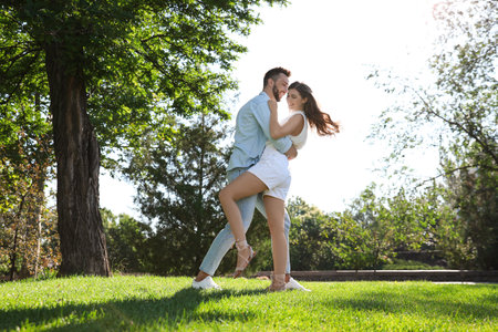 Lovely young couple dancing together in park on sunny dayの写真素材